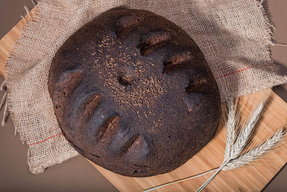 Dark rye loaf on sackcloth with ears of wheat
